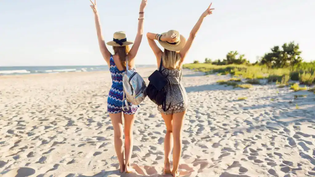 Two smiling women with raised hands on the beach in Koufonisia island, Greece