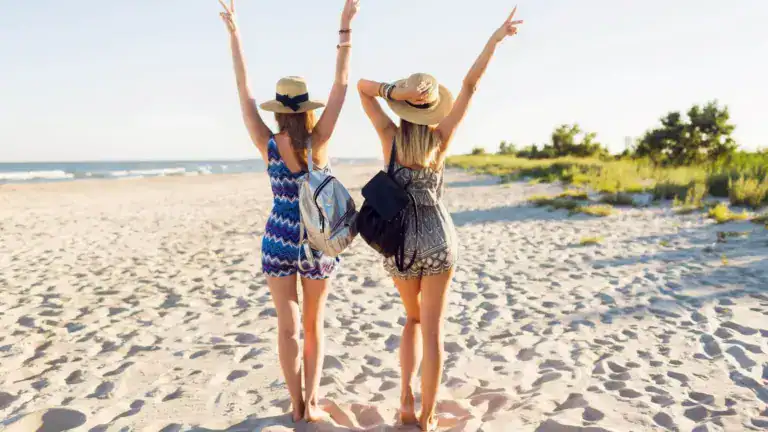 Two smiling women with raised hands on the beach in Koufonisia island, Greece